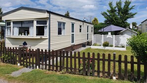 Une maison mobile avec une véranda, une cour clôturée et une antenne parabolique.