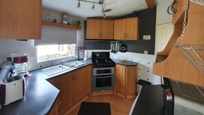 Une cuisine compacte avec des meubles en bois, un four encastré, une cuisinière et une fenêtre qui laisse entrer la lumière naturelle.