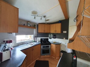 Eine kleine Küche mit Holzausstattung, einem eingebauten Backofen, einem Herd und einem Fenster für natürliches Licht.