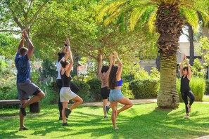 A group of people performing a yoga pose outdoors with trees and a palm tree in the background. - La Grande Motte "Le Ponant" (La Grande-Motte)