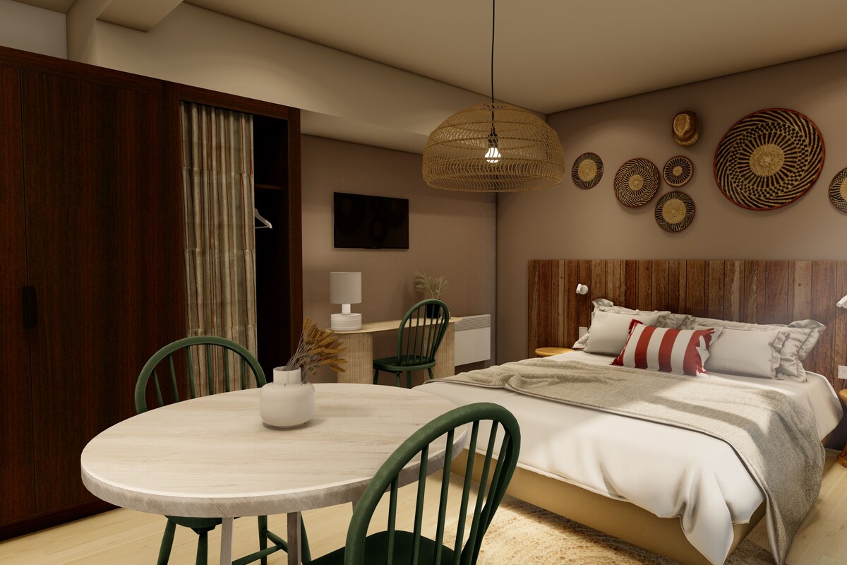 A modern bedroom with a wooden headboard, a round dining table with chairs, a hanging light fixture, and decorative wall art.