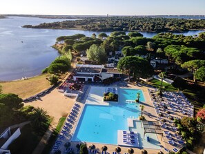 An aerial view of a resort with a large swimming pool, sun loungers, and a beach area.