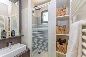 A bathroom with a glass-enclosed shower, a white sink, and shelves with wicker baskets. - La Grande Motte "Le Ponant" (La Grande-Motte)