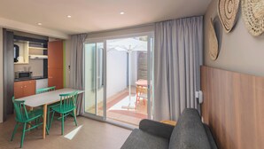 A modern apartment with a dining area, kitchenette, and a living room with a sofa and a sliding glass door to the outside.