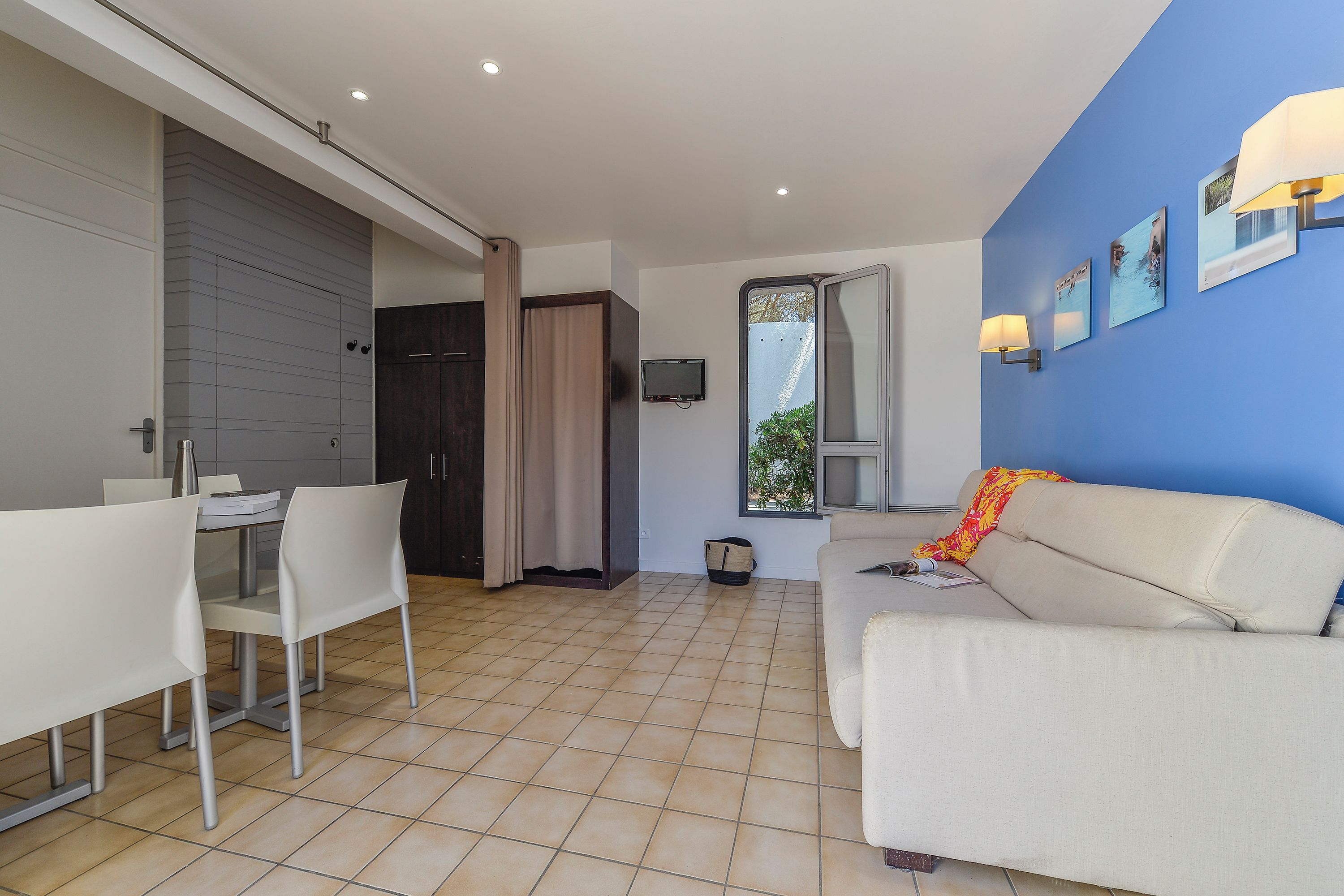 Un salon moderne comprenant un canapé, une table à manger avec des chaises, un téléviseur fixé au mur et une fenêtre donnant sur un paysage verdoyant.