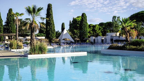 A swimming pool with lounge chairs, palm trees, and a white building with a conical roof.