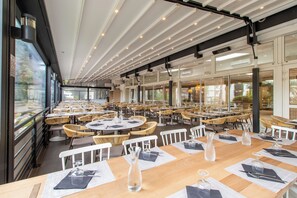 A spacious restaurant with round tables, wicker chairs, and large windows. - La Grande Motte "Le Ponant" (La Grande-Motte)