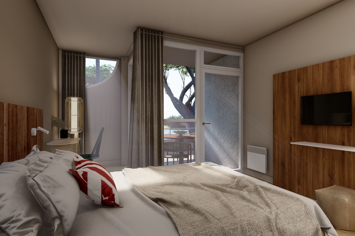 A modern hotel room with a large bed, a television mounted on a wooden wall, a small table with a lamp, and a view of the outdoors through a sliding door.