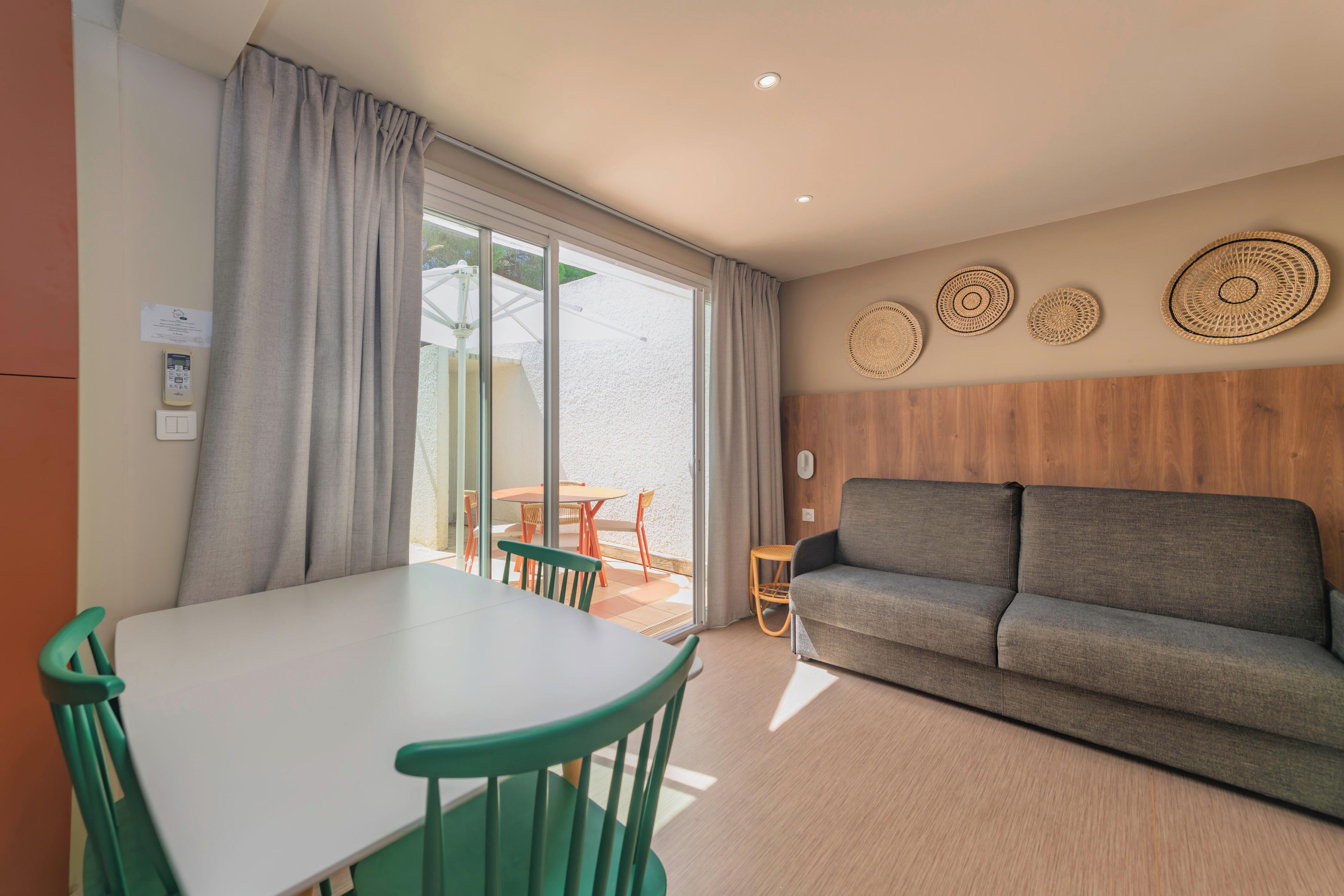 Une pièce moderne comprenant une table à manger, des chaises, un canapé et une porte-fenêtre coulissante donnant sur un espace extérieur.
