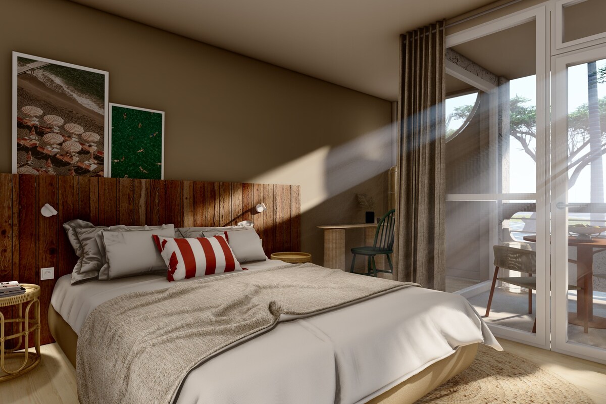 Une chambre à coucher avec une tête de lit en bois, un grand lit avec une literie blanche, une petite table d’appoint ronde, une chaise et une vue sur l’extérieur grâce à une porte vitrée.