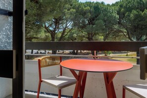 A balcony with a table and chairs, overlooking a park with trees. - La Grande Motte "Le Ponant" (La Grande-Motte)
