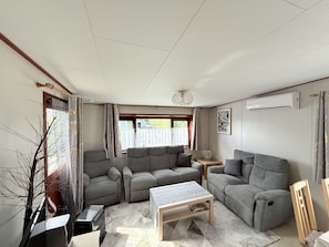 Ein Wohnzimmer mit einer Sofagarnitur, einem Couchtisch, einem Beistelltisch und einem Fenster mit Vorhängen.