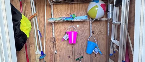A storage area with shelves holding various items like paint cans, a beach ball, and cleaning tools.