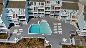 A multi-story hotel with balconies, a swimming pool, and outdoor seating areas. - Welcome to Sea Clearly, a newly remodeled first floor oceanfront condo in OIB (Ocean Isle Beach)
