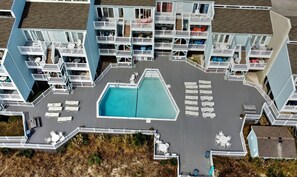 A multi-story hotel with balconies, a swimming pool, and outdoor seating areas. - Welcome to Sea Clearly, a newly remodeled first floor oceanfront condo in OIB (Ocean Isle Beach)