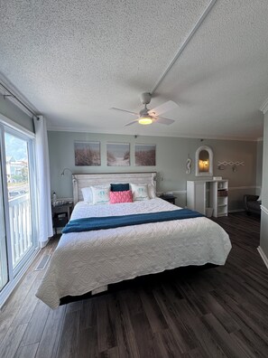 A bedroom with a bed, a ceiling fan, a window, and a view of the outside. - Welcome to Sea Clearly, a newly remodeled first floor oceanfront condo in OIB (Ocean Isle Beach)
