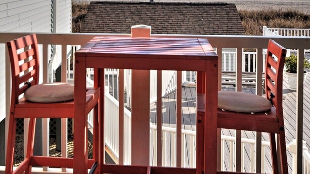 A balcony with a table and chairs overlooking a beach with a ship in the distance. - Welcome to Sea Clearly, a newly remodeled first floor oceanfront condo in OIB (Ocean Isle Beach)