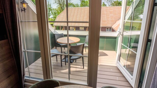 Una habitación con un amplio ventanal corredero que da a una terraza exterior con mesa y sillas.