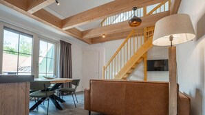 Un interior moderno con una escalera de madera, un sofá, una mesa de comedor con sillas y un televisor montado en la pared.