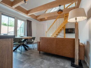 Ein modernes Interieur mit einer Holztreppe, einem Sofa, einem Esstisch mit Stühlen und einem an der Wand montierten Fernseher.
