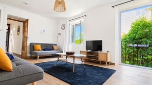 Un salon moderne avec un canapé, une table basse, un téléviseur et une vue sur la verdure à l’extérieur.