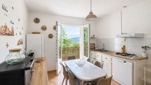 Une cuisine compacte avec un coin repas, une vue à travers la porte ouverte et un petit îlot central surmonté d’un bocal en verre.