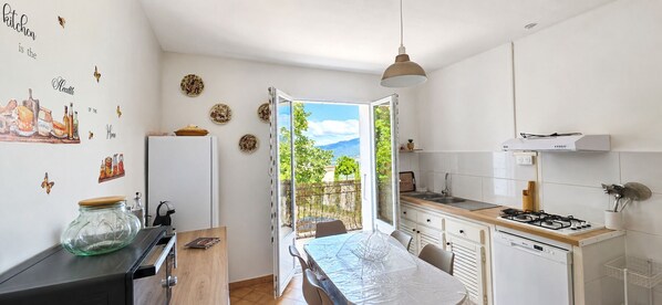 A compact kitchen with a dining area, a view through an open door, and a dining table with chairs.