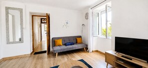 A living room with a sofa, a television, a wooden cabinet, and a window.
