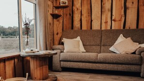 A cozy room with a wooden wall, a grey sofa with pillows, a small round table with a vase and books, and a woven basket on the floor. - Hoeve Twente - De Bosuil by Interhome (Heythuysen)