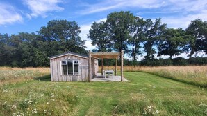 A small wooden cabin with a covered patio area, surrounded by a grassy field and trees. - Hoeve Twente - De Bosuil by Interhome (Heythuysen)
