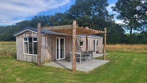 A rustic wooden cabin with a covered patio, large windows, and a door. - Hoeve Twente - De Bosuil by Interhome (Heythuysen)