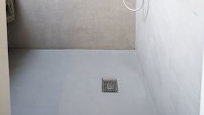 Una ducha con cabezal de ducha de mano, grifo empotrado en la pared y un espejo redondo.