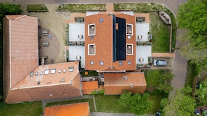 Vista aérea de un edificio con varias secciones de techo, zonas de estar al aire libre y un estacionamiento.