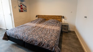 Un dormitorio con cama, mesita de noche, lámpara, una obra de arte en la pared y una puerta.