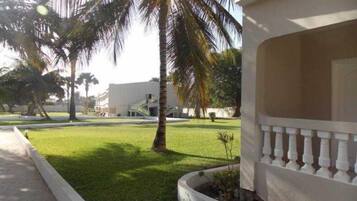 A well-maintained lawn, a white building with a balcony, and palm trees in a sunny outdoor setting.