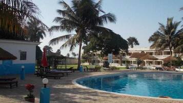 A pool area with palm trees, lounge chairs, and a building with a thatched roof.