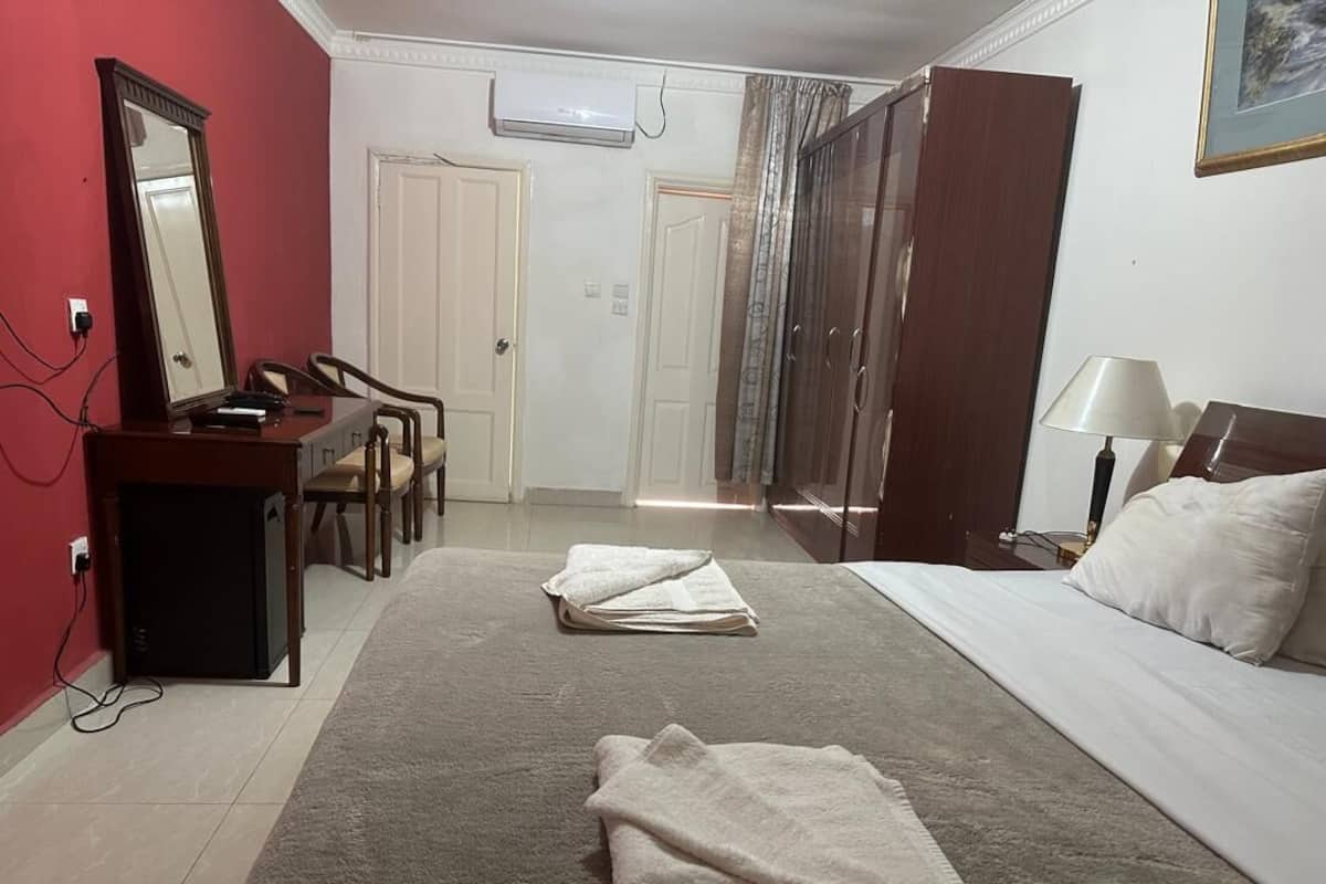 Ein Hotelzimmer mit Bett, Schreibtisch mit Spiegel, Stuhl, Kleiderschrank und Lampe.