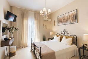 Ein Hotelzimmer mit Bett, Fernseher, einer Kronleuchter, einem Gemälde und einer Pflanze.
