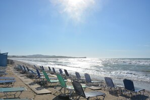 A beach with rows of sun loungers and a clear view of the ocean. - V.a. Boutique Apartments and Suites (Corfu)