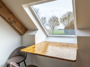 Ein Zimmer mit schrägen Wänden, einem Oberlicht, einem Holztisch und einem Stuhl.