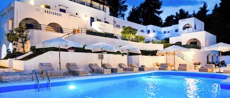A large outdoor swimming pool with lounge chairs and umbrellas, surrounded by a multi-story building with balconies and stairs.