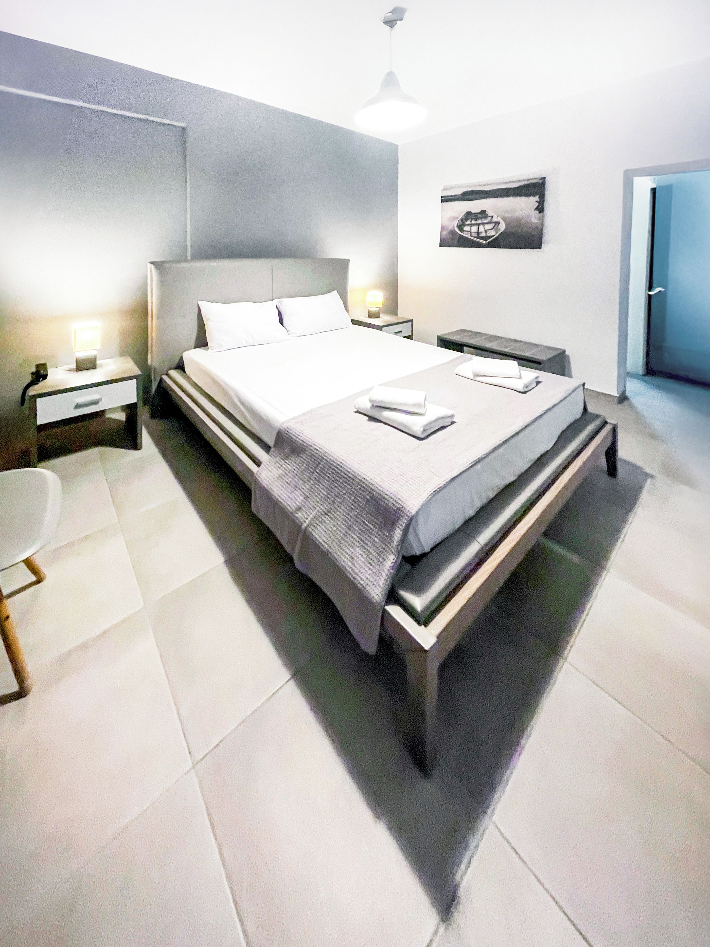 Ein modernes Schlafzimmer mit einem großen Bett, Nachttischen, einem Beistelltisch und einem an der Wand hängenden Kunstwerk.