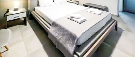 Ein modernes Schlafzimmer mit einem großen Bett, Nachttischen, einem Beistelltisch und einem an der Wand hängenden Kunstwerk.