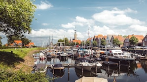 Ein Yachthafen mit vertäuten Booten, eine Kirche mit Turm und traditionelle Gebäude mit roten Dächern.