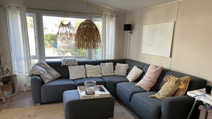 Ein modernes Wohnzimmer mit einem dunkelgrauen Ecksofa, einem gewebten Teppich und einem großen Fenster mit Vorhängen.
