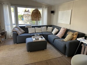 Ein modernes Wohnzimmer mit einem dunkelgrauen Ecksofa, einem gewebten Teppich und einem großen Fenster mit Vorhängen.