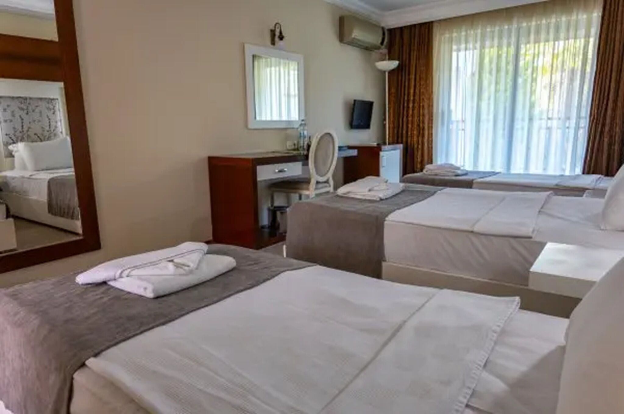 A hotel room with two beds, a desk with a mirror, a TV, and a window with curtains.