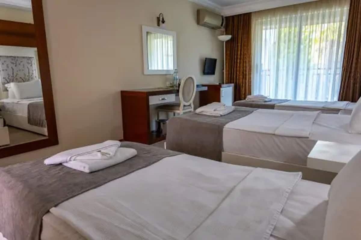 A hotel room with two beds, a desk with a mirror, a TV, and a window with curtains.