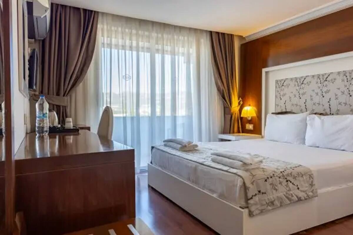 A hotel room with a bed, a desk, a chair, a lamp, and a window with curtains.