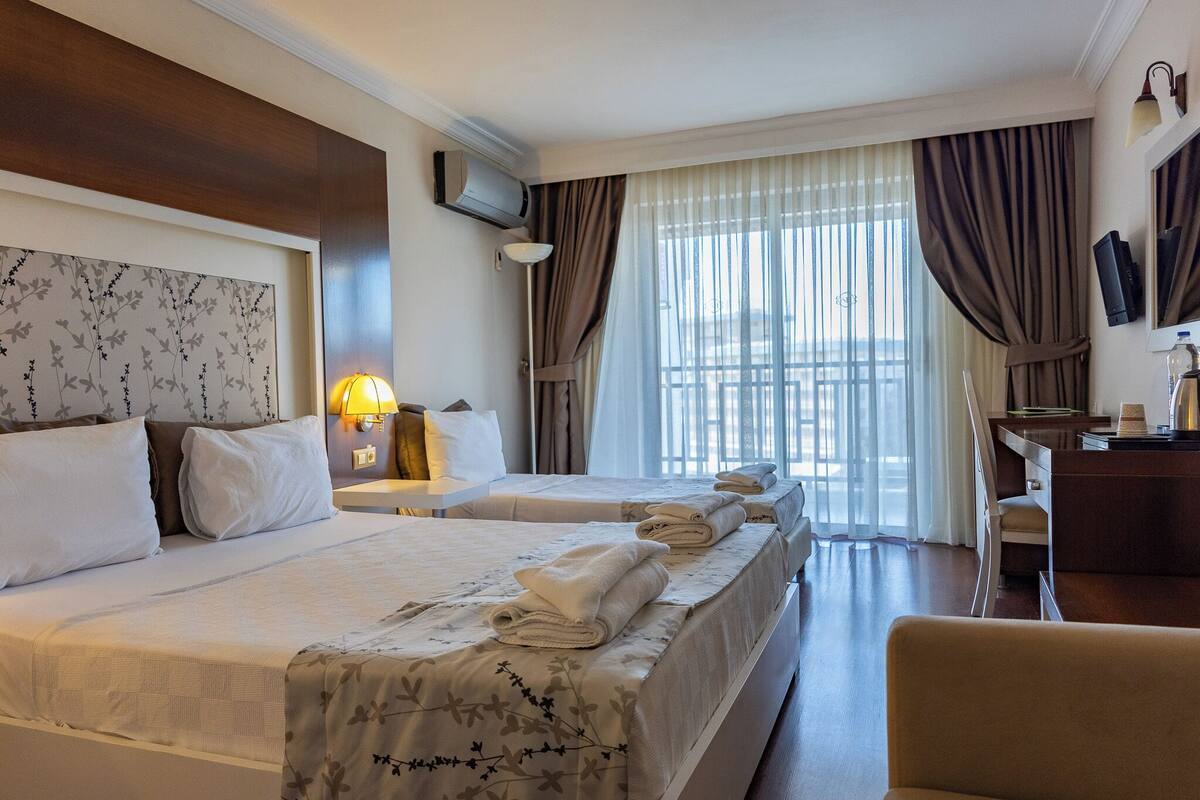 A hotel room with two beds, a desk, a chair, a TV, and a window with curtains.